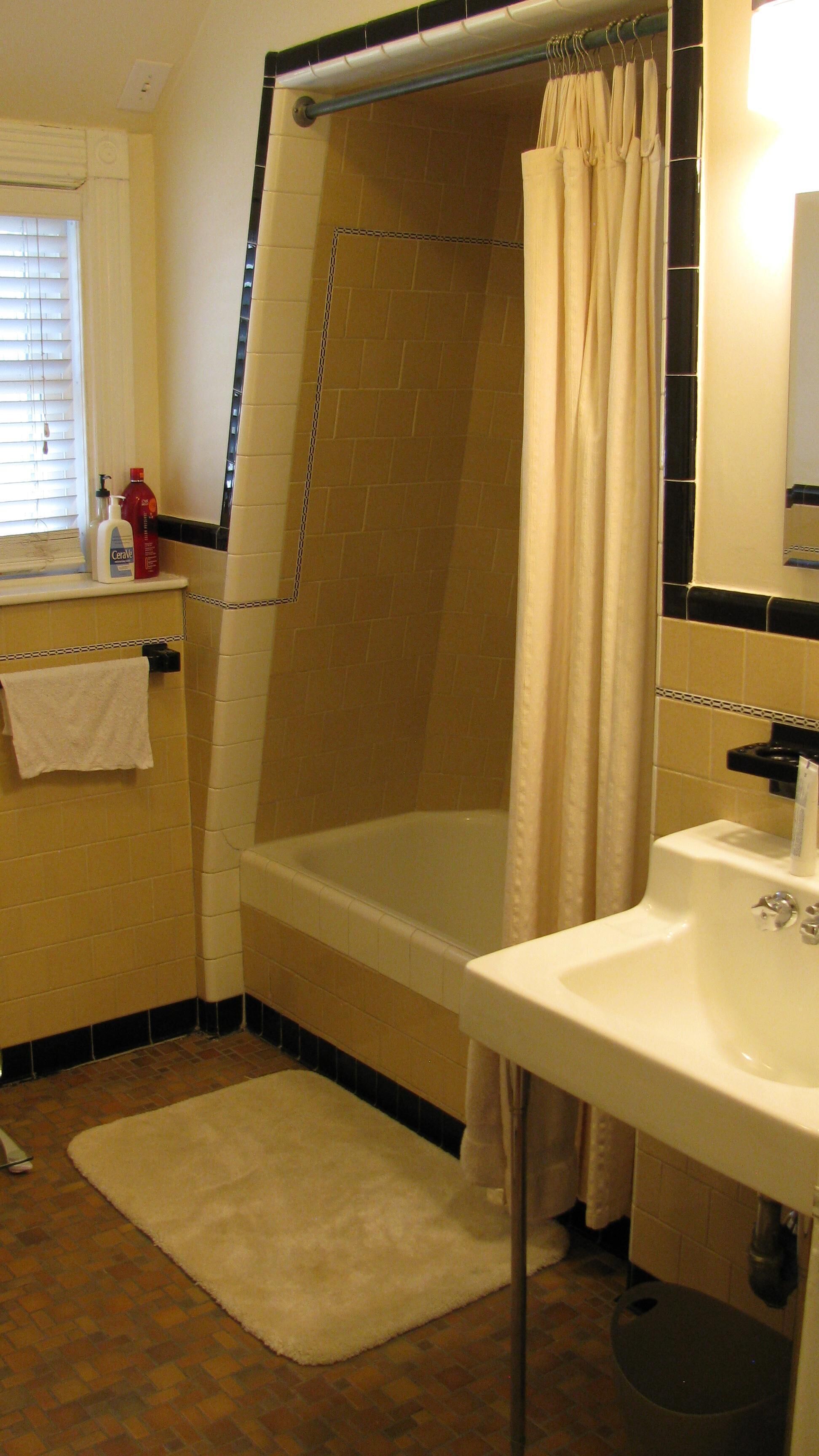 A bathroom with a bathtub, a sink, and a window with blinds.