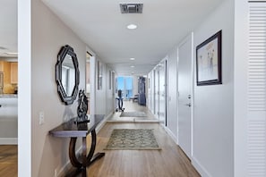 A hallway with a wooden floor, a mirror, a rug, and framed pictures on the walls. - 2/2 Beachfront, VIEWS, Pool, Private Beach Access (Longboat Key)