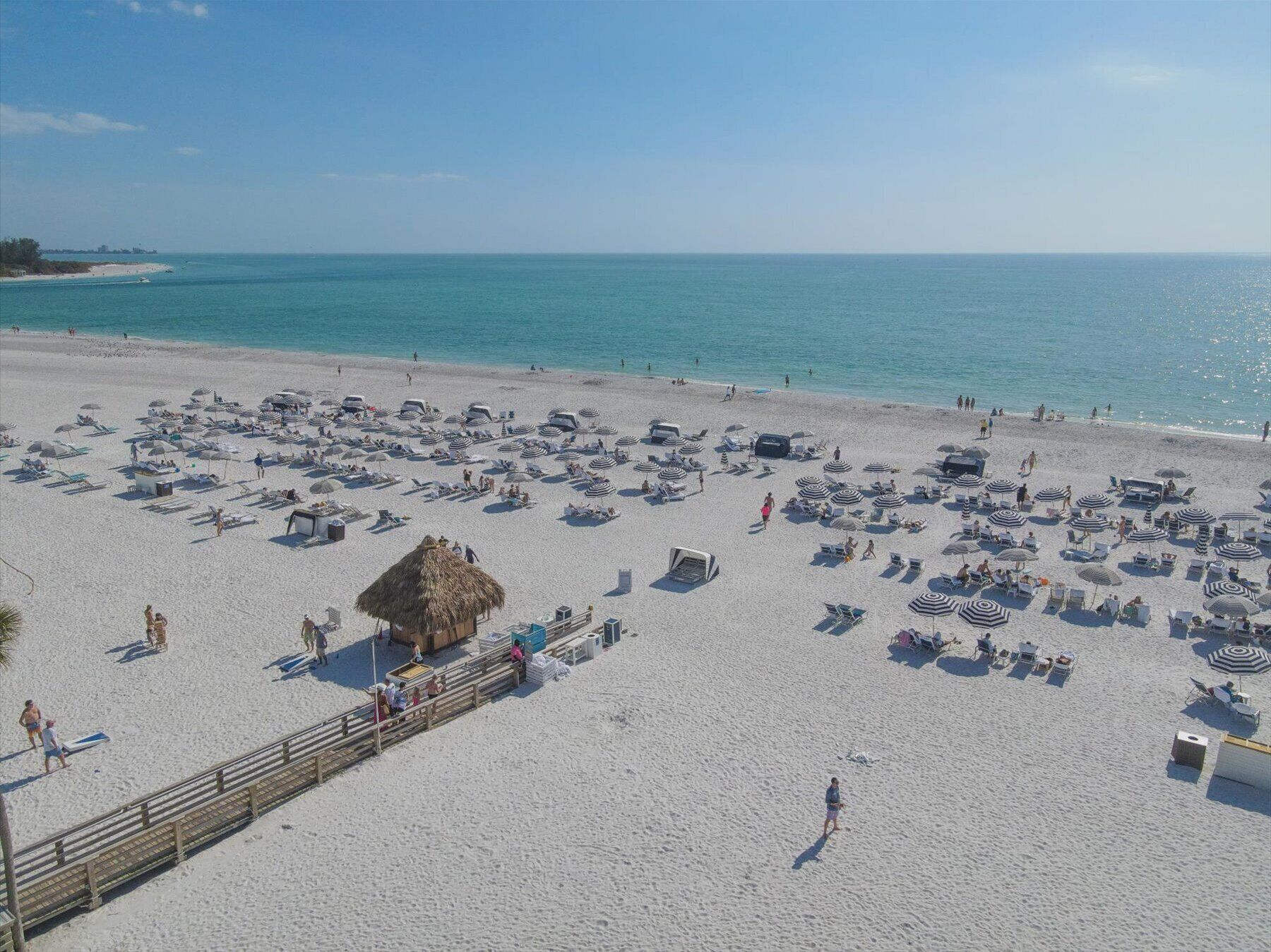 A beach with numerous sun loungers and umbrellas, a wooden pier, and a thatched-roof hut.
