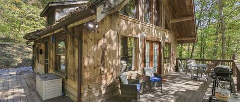 A wooden cabin with a deck, outdoor seating, and a grill.