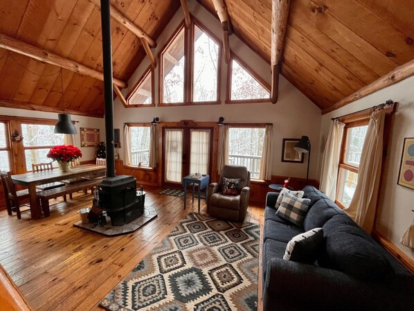 Een gezellig cabin interieur met een houten vloer, een open haard, een bank, een eettafel en grote ramen.