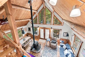 A rustic cabin interior with a large fireplace, wooden furniture, and multiple windows offering views of the surrounding forest. - A couple's get-away in the woods. (Nelsonville)