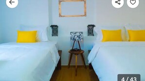 Een kamer met twee bedden, elk voorzien van een geel kussen en witte beddengoed. Tussen de bedden staat een klein tafeltje met een lamp.