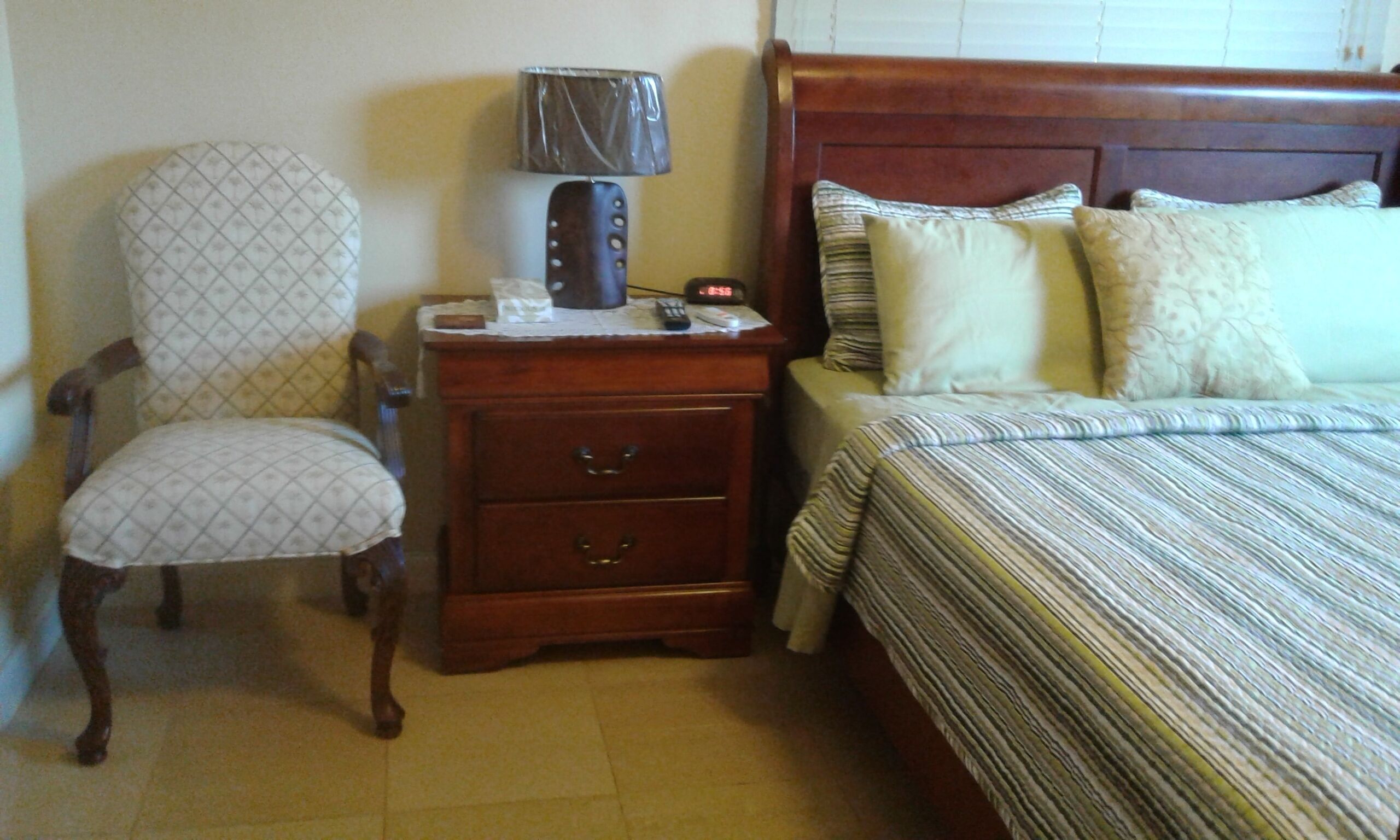 A bedroom with a wooden nightstand, a chair, a bed with striped bedding, and a lamp.