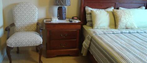 A bedroom with a wooden nightstand, a chair, a bed with striped bedding, and a lamp.