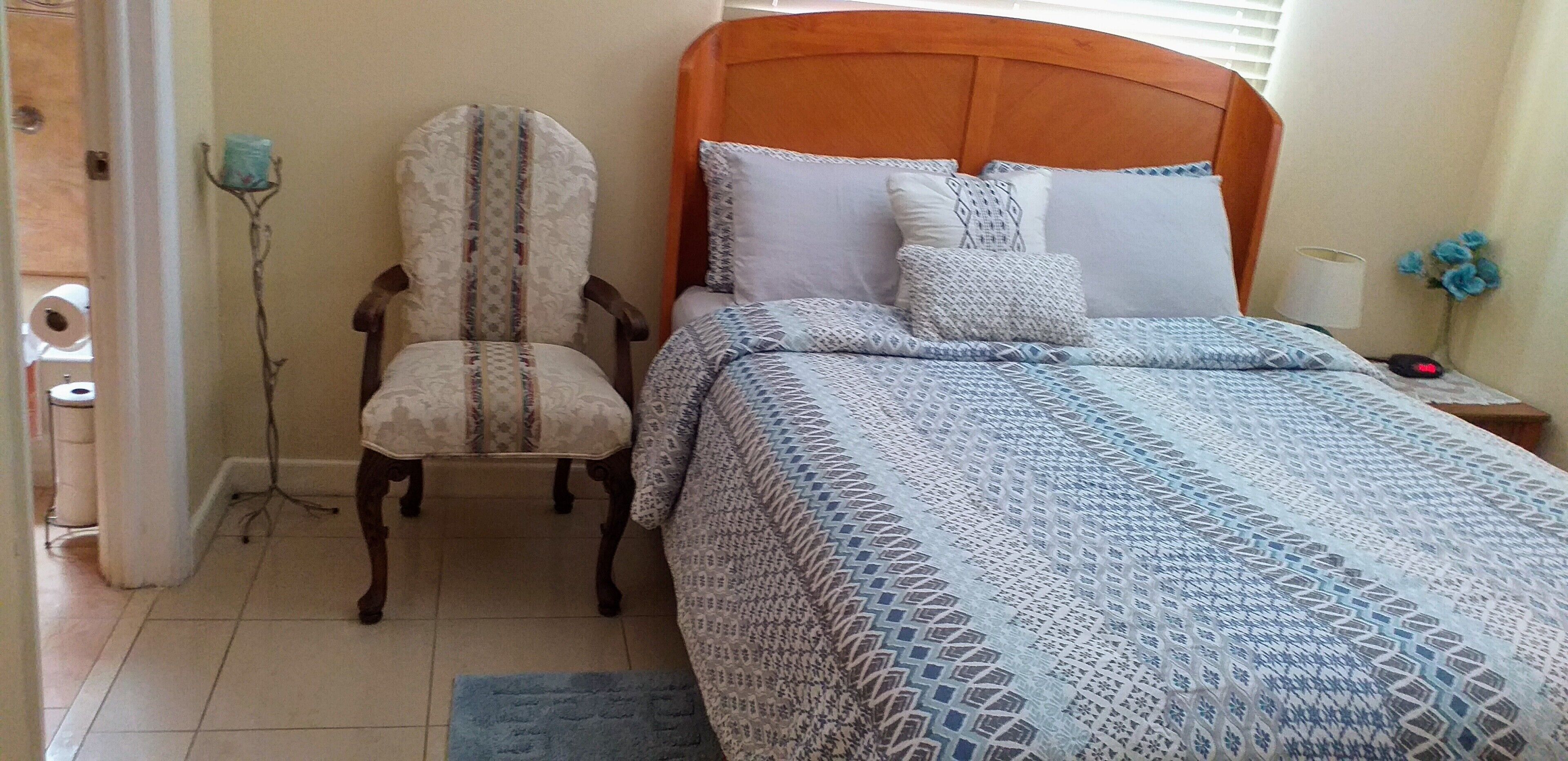 A bedroom with a bed, a chair, a nightstand, and a lamp.