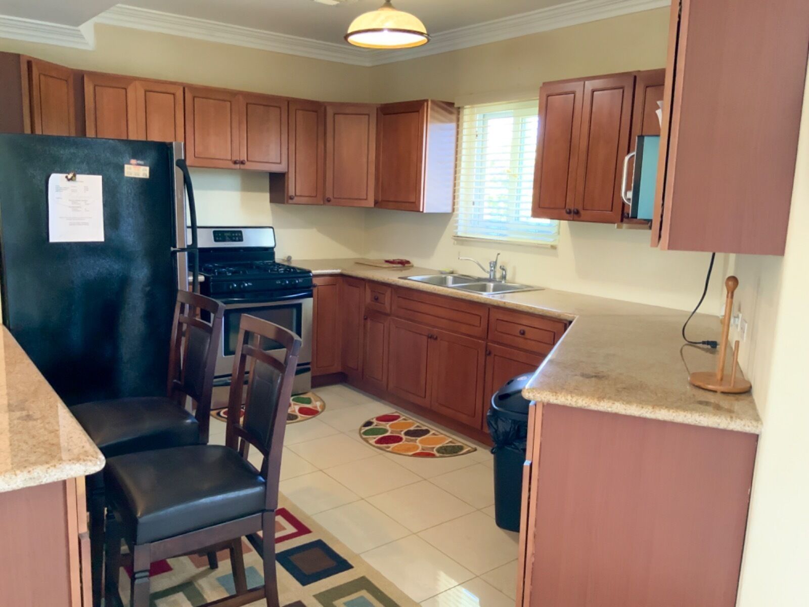 A kitchen with wooden cabinets, a refrigerator, a stove, a sink, and a dining area with chairs.