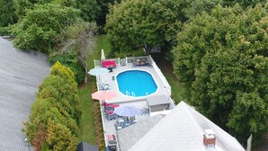 An aerial view of a backyard with a swimming pool, surrounded by trees and a deck with outdoor furniture. - Jamestown: Cozy Coastal Cottage in town near beaches & Newport, dogs OK! (Jamestown)