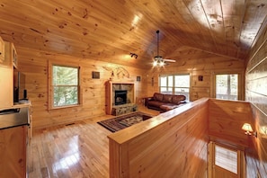 A wooden cabin interior with a fireplace, a sofa, and a ceiling fan. - Above the Rest| 2BR| Helen| Hot tub & Mountain views (Helen)