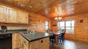 A wooden cabin interior with a kitchen, dining area, and a large window.