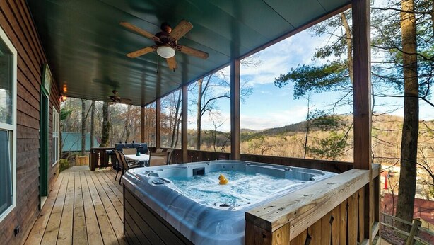 A wooden deck with a hot tub, a ceiling fan, and a view of the surrounding landscape.