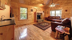 A cozy cabin interior with wooden walls, a fireplace, a leather sofa, and a dining area.