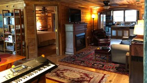 A cozy cabin interior with a wooden floor, a fireplace, a television, a piano, and a kitchen area. - Unique farm guest house close to Chattanooga, TN- great for families and dogs (Chickamauga)
