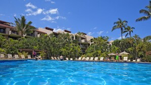 Un hôtel doté d’une piscine entourée de palmiers et de chaises longues.