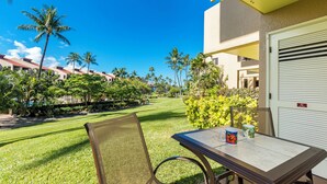 Un balcon avec une table, une chaise et une vue sur une pelouse bien entretenue et des palmiers.