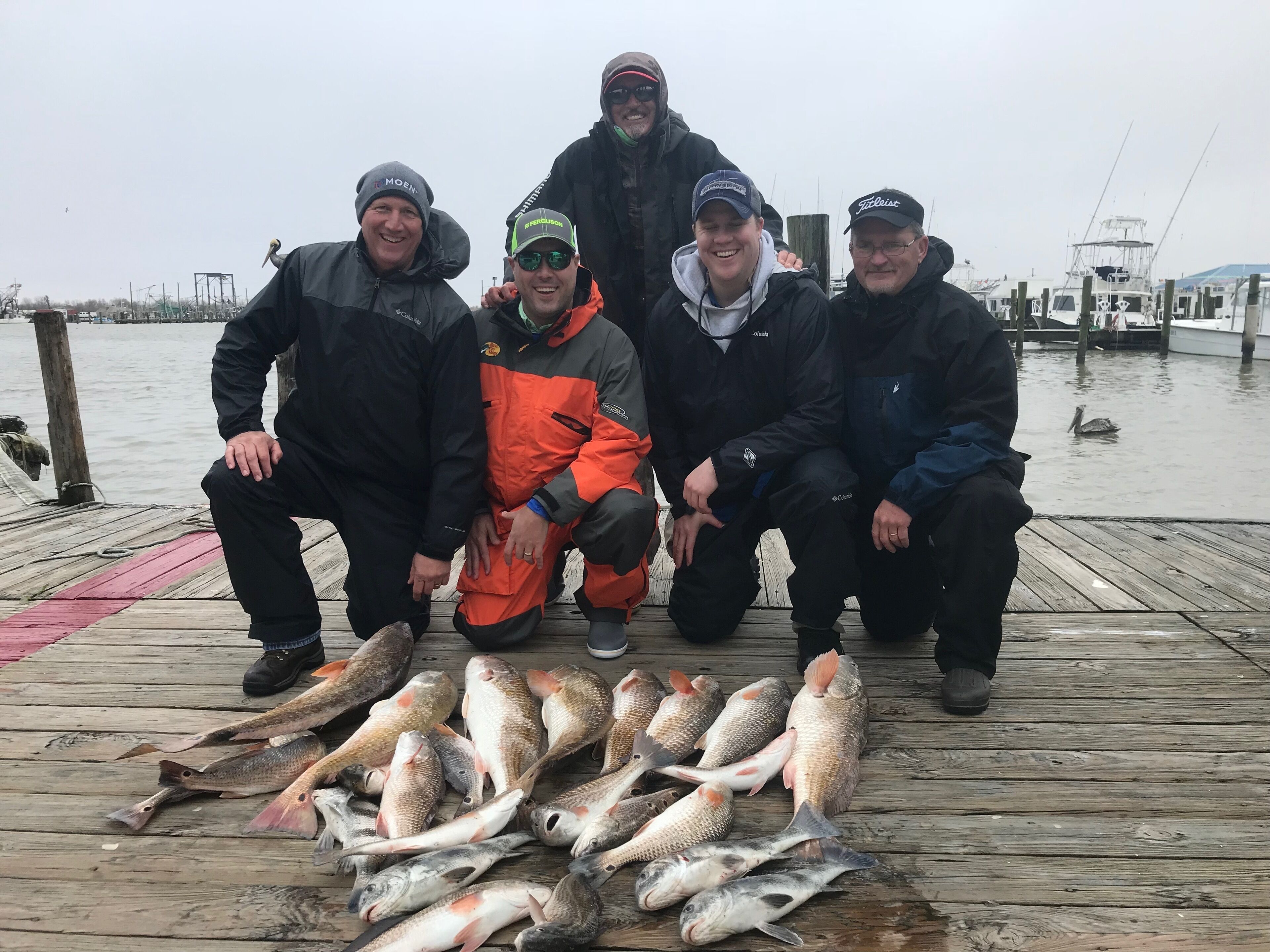A group of people on a wooden dock with several fish laid out in front of them.