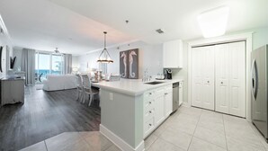 A modern kitchen with a central island, white cabinetry, and a dining area with a white sofa and chairs. - Waterscape A506  ~ Beach Service ~ Amazing View! (Fort Walton Beach)