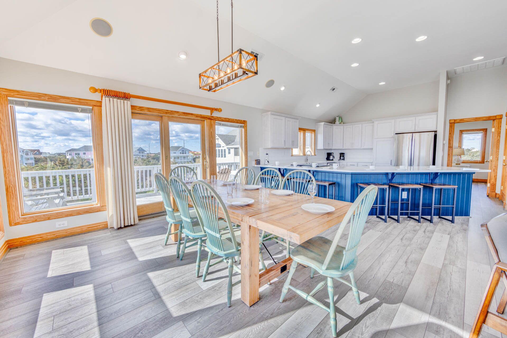 Una cocina moderna con armarios blancos, una isla azul y una zona de comedor con mesa y sillas de madera.