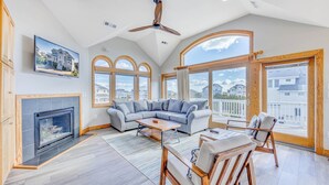A spacious living room with a fireplace, a large gray sectional sofa, a wooden coffee table, and a ceiling fan. - Oceanview Dog Friendly Home w/ Pool, Hot Tub, Elevator, Game and Media Rooms (Avon)