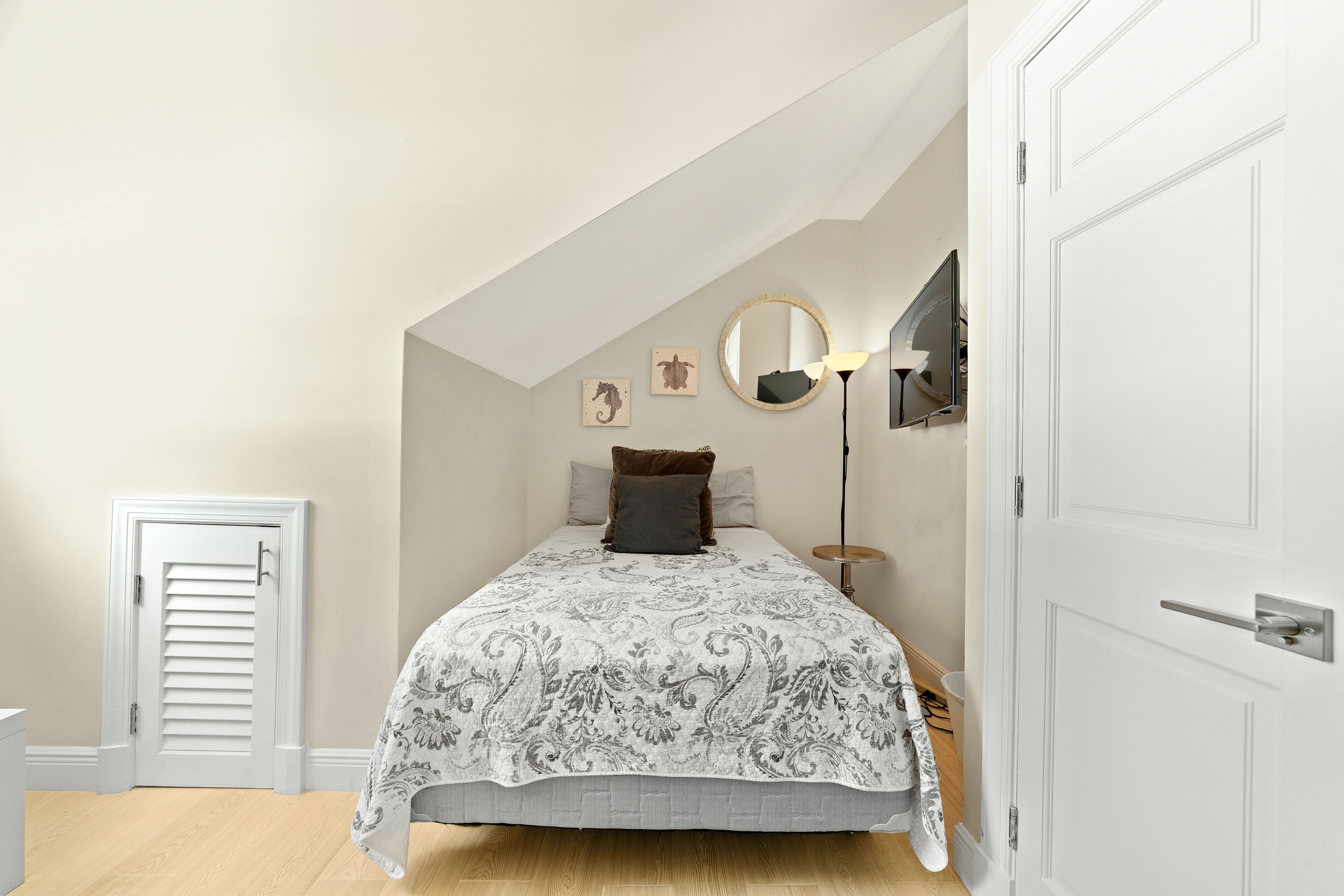Un dormitorio con cama, mesita de noche, lámpara y puerta.