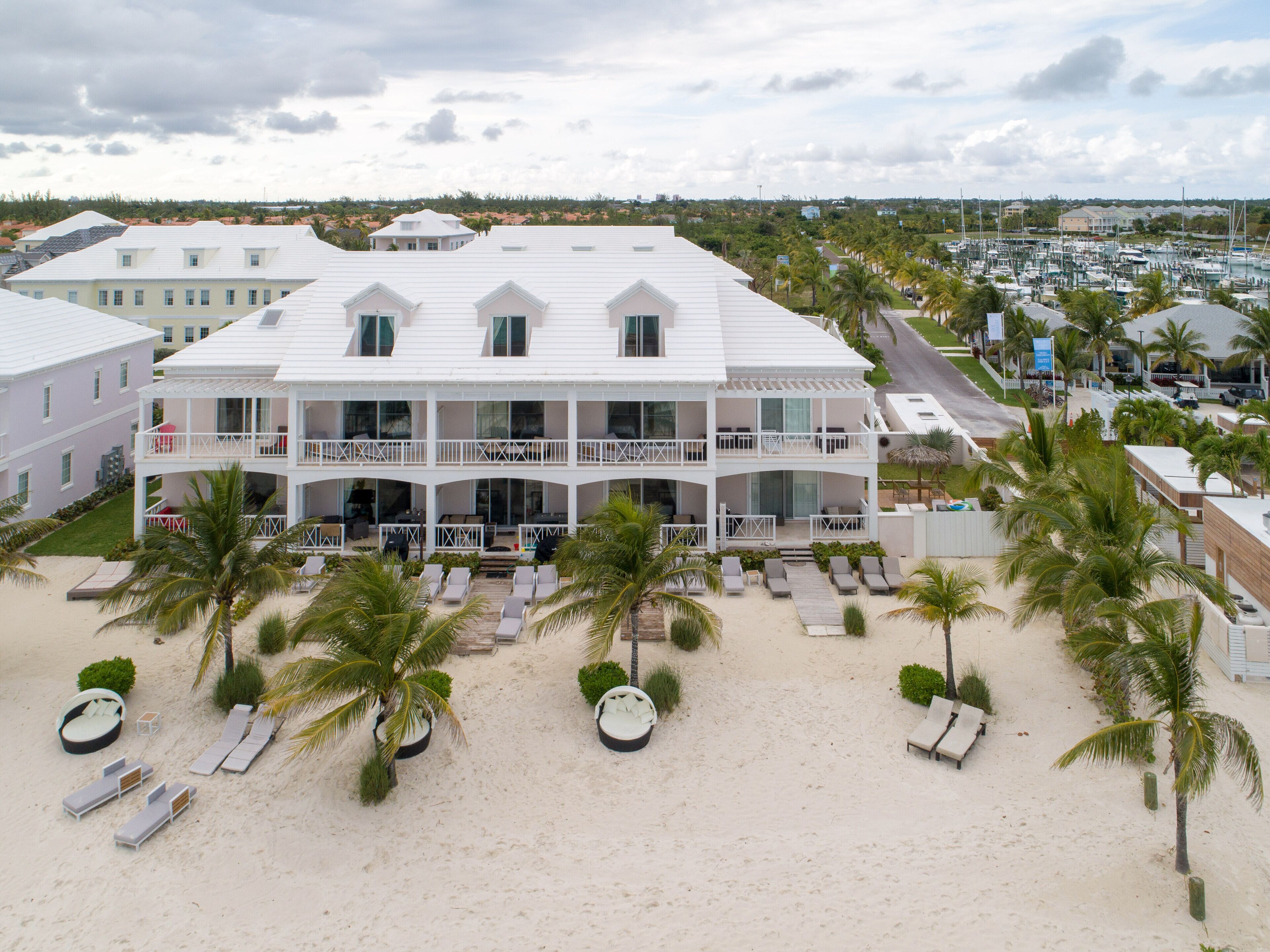 Un grand immeuble à plusieurs étages, doté d’une façade blanche, de nombreux balcons et situé en bord de mer, avec des chaises longues et des palmiers.
