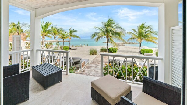 Un espacio de estar al aire libre techado con muebles de mimbre, vista a la playa y palmeras.