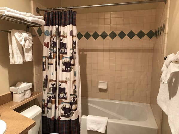 Un baño con cortina de ducha estampada con motivos de animales salvajes, una bañera y un perchero con toallas dobladas.