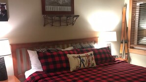 A bed with a red and black checkered bedspread, flanked by pillows, in a room with a wooden headboard and a framed picture above.