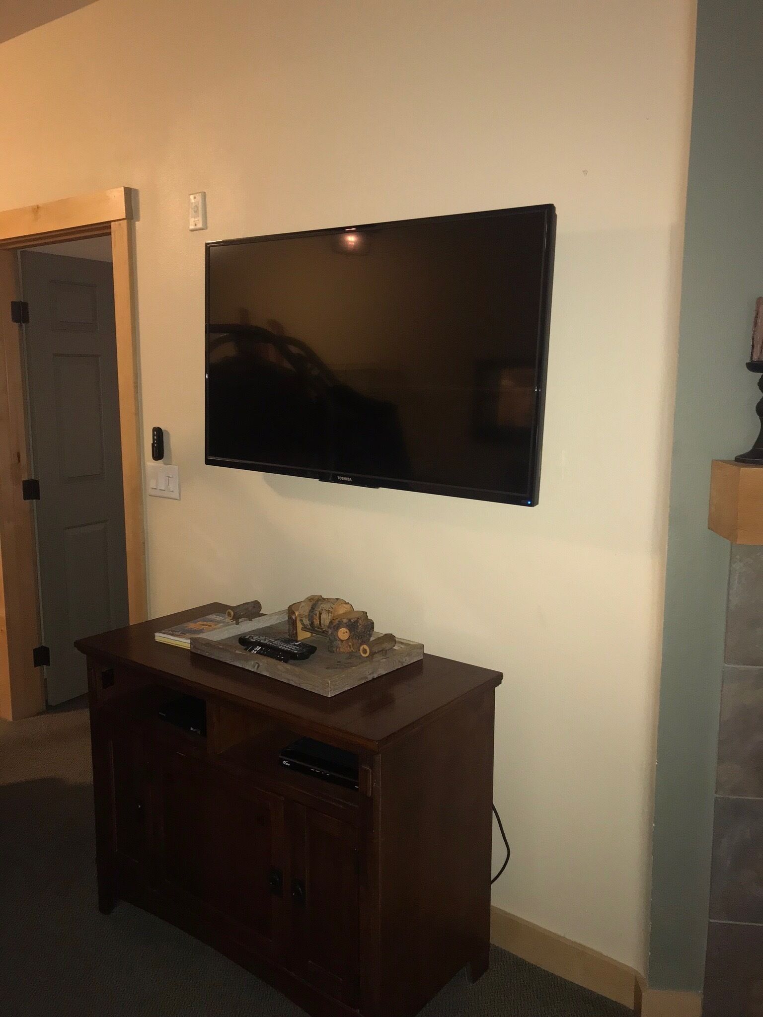 Een flatscreen televisie bevestigd aan een muur boven een houten kastje, met een afstandsbediening en een boek erop.