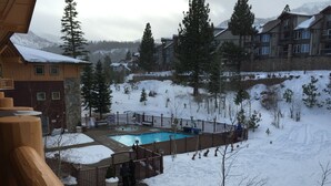 A pool area surrounded by a wooden fence, with snow-covered ground and buildings in the background.
