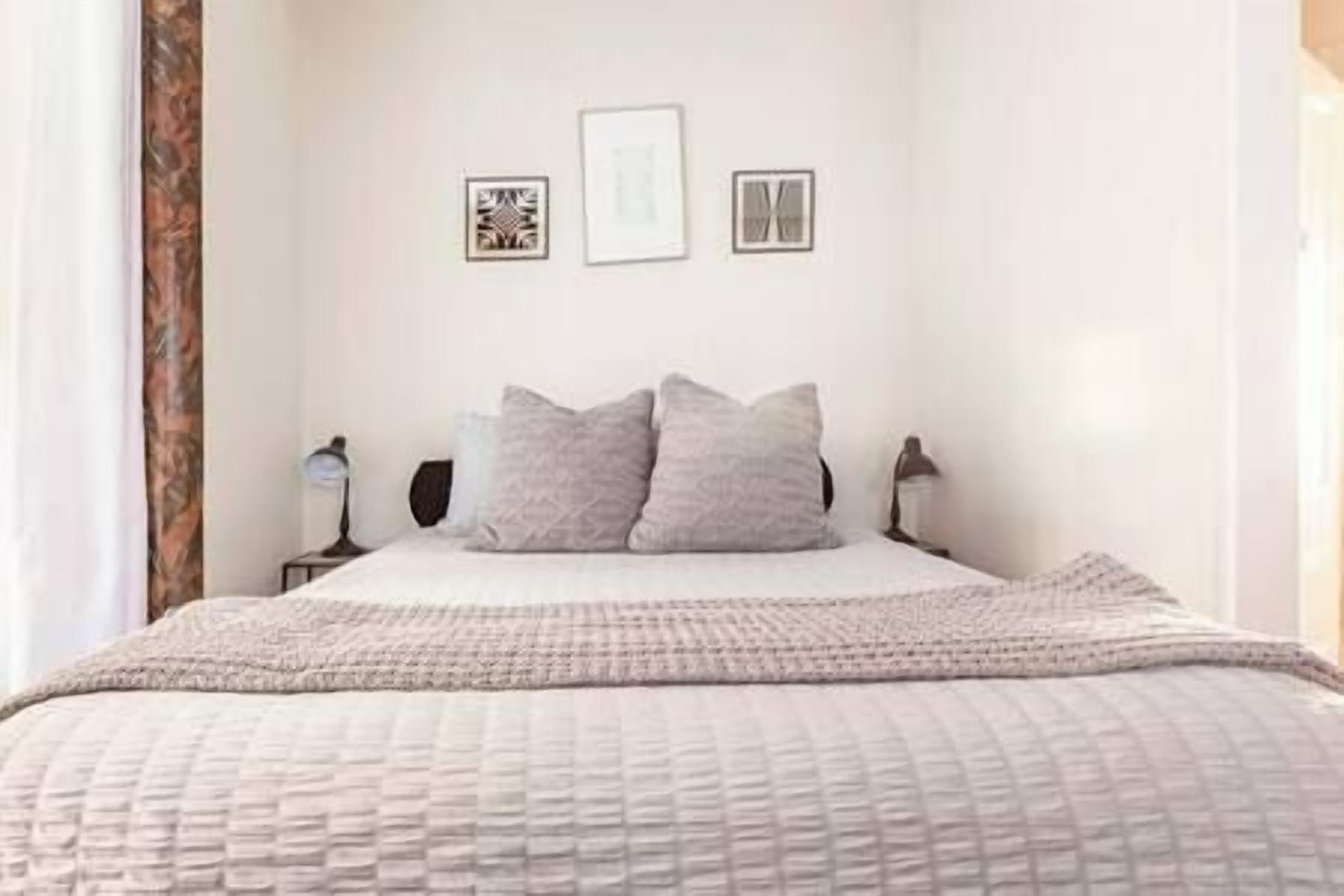 A bedroom with a bed, two bedside lamps, a bedside table, and a wall with three framed pictures.