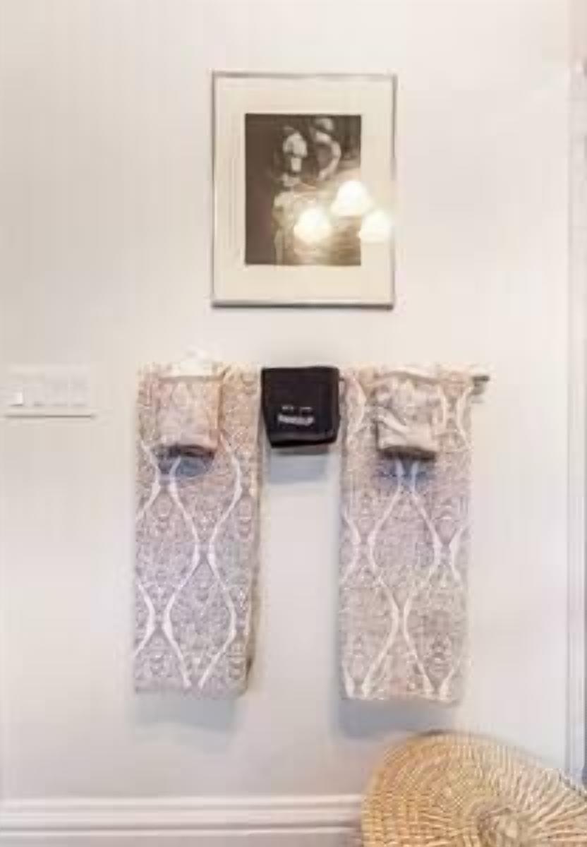 A wall with a framed photograph, two patterned towels, and a small black object.