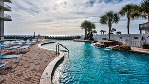 A swimming pool with lounge chairs, palm trees, and a view of the ocean. - 1 Bedroom in Majestic Beach Resort - Low floor, Spacious and bright and beautifully decorated! (Panama City Beach)