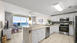 A modern kitchen with white cabinets, a large island, stainless steel appliances, and a view to the outside. - 1 Bedroom in Majestic Beach Resort - Low floor, Spacious and bright and beautifully decorated! (Panama City Beach)