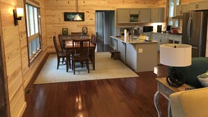 A cozy log cabin interior with a dining area, kitchen, and a living space.