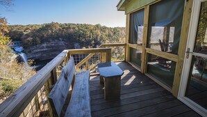 A wooden deck with a bench and table, overlooking a waterfall and forested area.