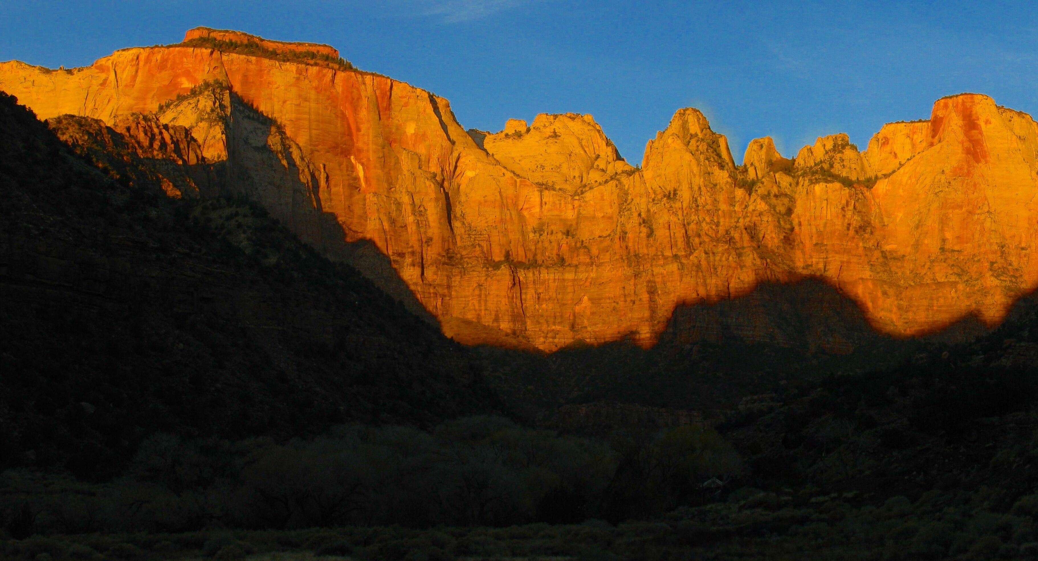 A mountain landscape with a prominent cliff face and a clear sky.