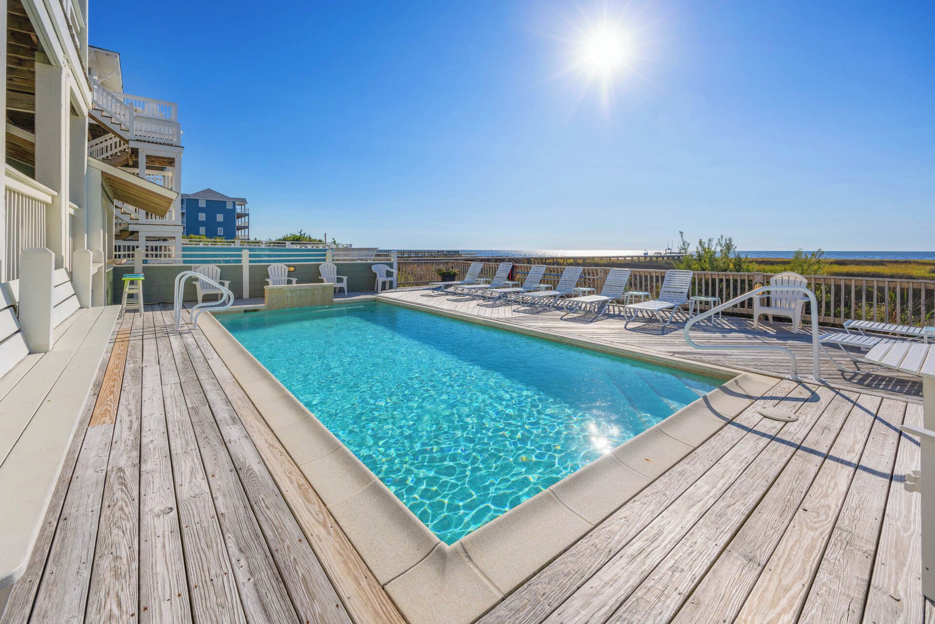 Une terrasse en bois avec une piscine, des chaises longues et une vue sur l’océan.