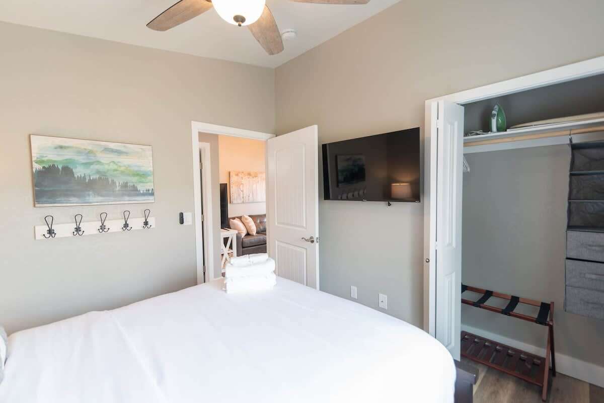 A bedroom with a bed, a ceiling fan, a TV, a coat rack, and a door leading to another room.