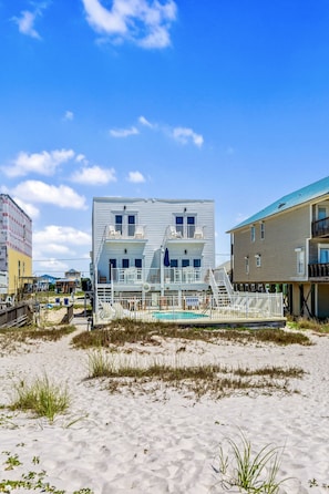 Een tweelaags gebouw aan het strand met een zwembad, omgeven door zand en gras.