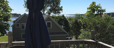 En terrass med ett glasbord och flätade stolar, med utsikt över ett bostadsområde och en vattenyta.