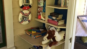 A room with a bookshelf containing books and a stuffed toy. There are life preservers hanging on the wall.