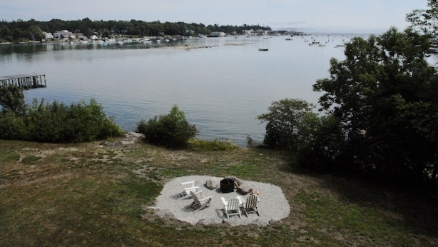 A lakeside view with a sandy area featuring outdoor seating and a fire pit.