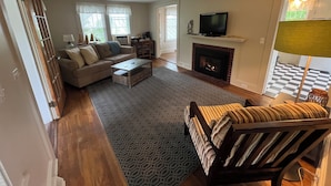 A living room with a sofa, coffee table, fireplace, television, and patterned rug.