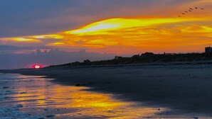 Una playa al atardecer, con el sol poniéndose en el horizonte, reflejándose en la arena húmeda.