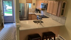 A kitchen with a stainless steel refrigerator, a microwave, and a sink. There are wooden cabinets and a window with blinds. - Top Rated Creekside Gem Is Steps From Free Bus To Skiing, Shopping, & Dining! (Vail)
