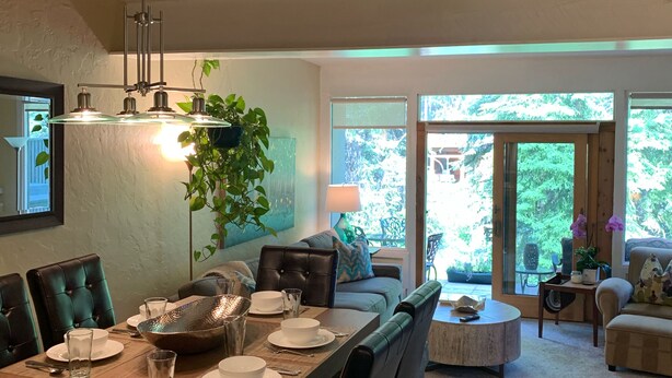 A dining area with a wooden table set for four, surrounded by leather chairs. There is a large window with a view of greenery outside. - Top Rated Creekside Gem Is Steps From Free Bus To Skiing, Shopping, & Dining! (Vail)