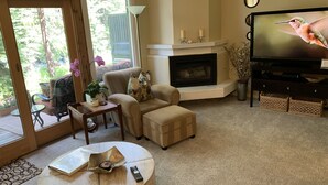 A cozy living room with a fireplace, comfortable seating, a television, and a view of the outdoors. - Top Rated Creekside Gem Is Steps From Free Bus To Skiing, Shopping, & Dining! (Vail)