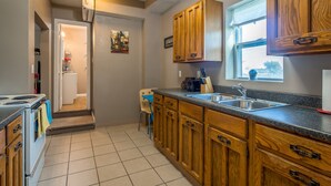 Una cocina con armarios de madera, un fregadero y una estufa. Hay una ventana sobre el fregadero y una puerta que da a otra habitación.