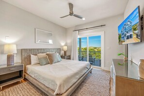 A bedroom with a bed, nightstands, a ceiling fan, a large window with a view, and a TV on the wall.